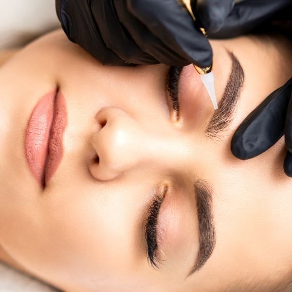 Cosmetic tattoo artist performing microblading procedure on a client’s eyebrows.