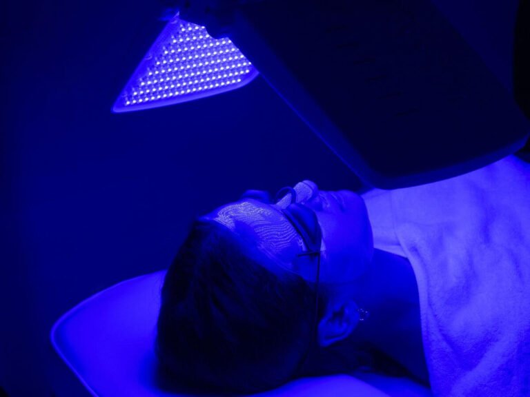 Client receiving acne treatment with blue LED therapy and high frequency to target acne-causing bacteria.